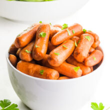 A bowl of roasted carrots has parsley on top and around it. There's a bowl of salad behind it.