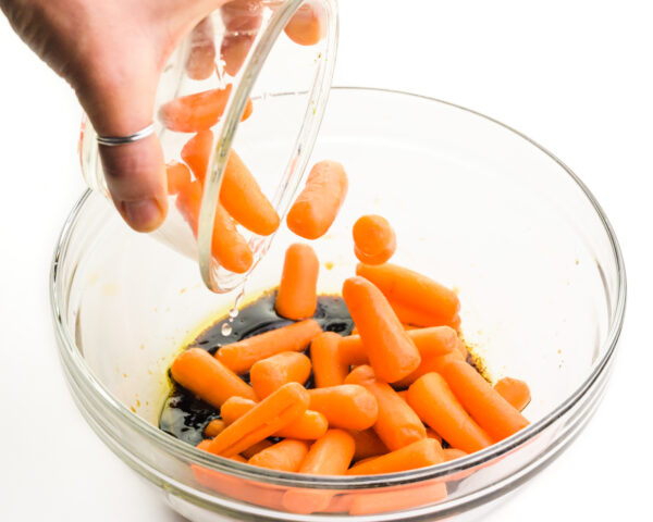 Baby carrots are being tossed into a bowl with a balsamic mixture.