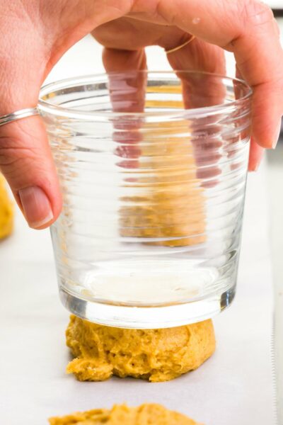 A hand holds a glass and is pressing it down on cookie dough.