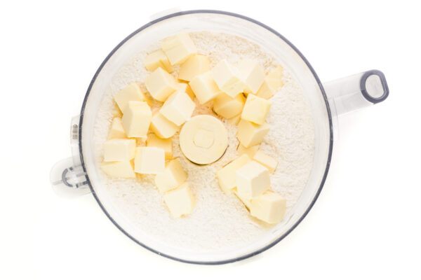 Vegan butter cubes have been added to a food processor bowl with a flour mixture.
