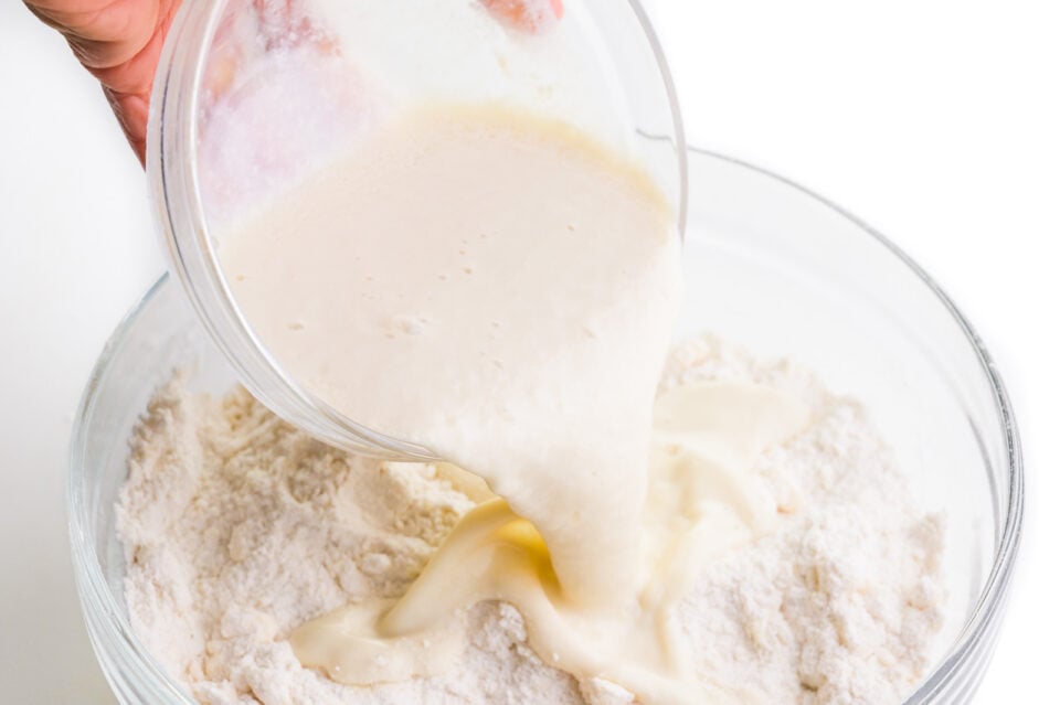 Vegan buttermilk is being poured into a bowl full of flour.