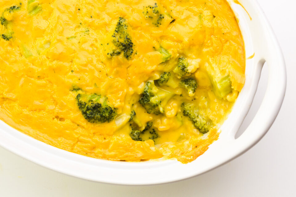 Looking down into a casserole dish full of a a cheesy broccoli mixture, with a bite or two taken out of it.