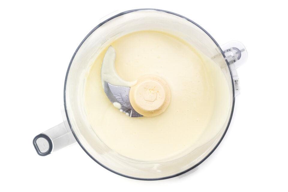 A mixture of soy milk and other ingredients are in the bottom of a food processor bowl.