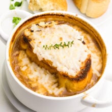 Looking down on a bowl of onion soup with a sprig of fresh thyme on the top and melted cheese.