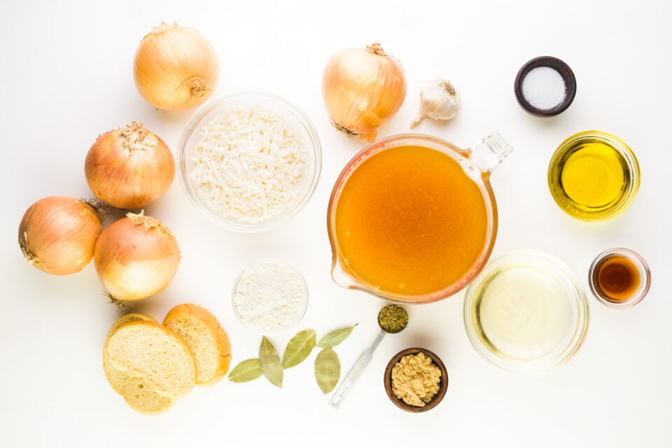Ingredients are lined up on a white counter. There's onions, broth, olive oil, flour, bay leaves, and more.