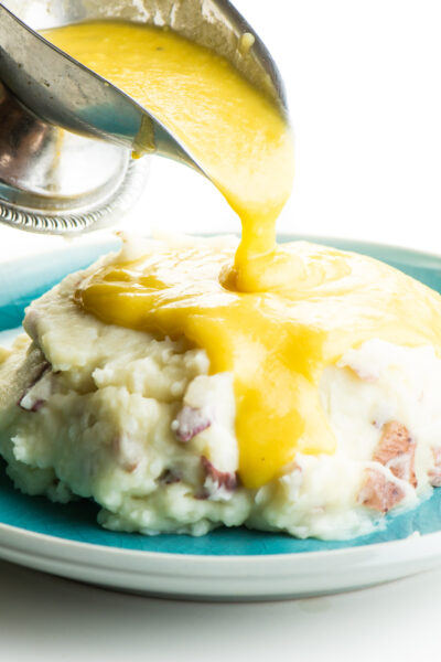 Vegan gravy is poured over a big plate of mashed potatoes.