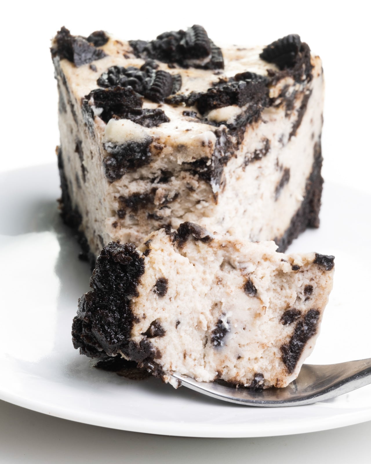 A bite of cheesecake is on a fork resting on a plate in front of the rest of the slice.