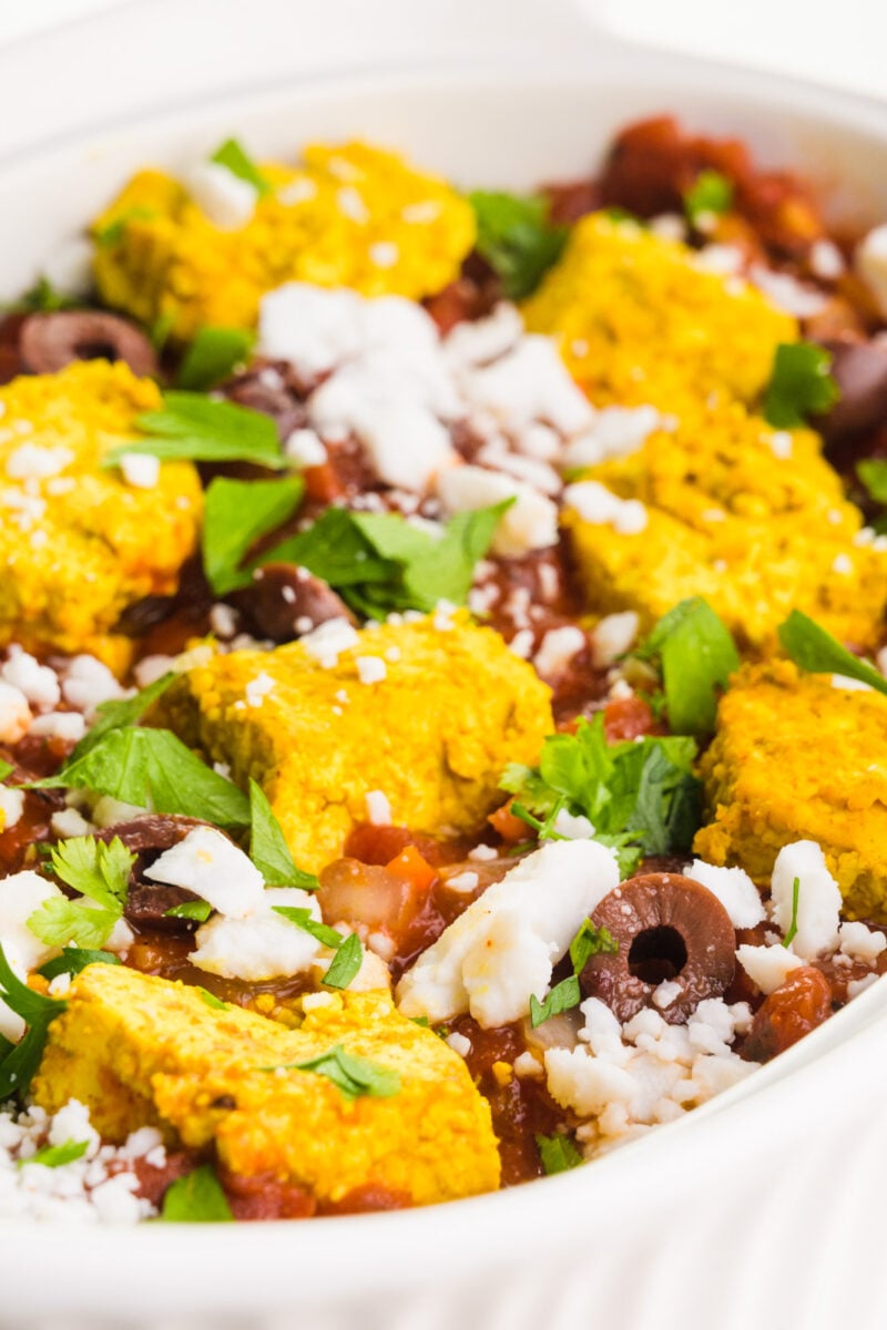 A close-up of a tomato casserole dish with tofu on top and vegan feta crumbles.
