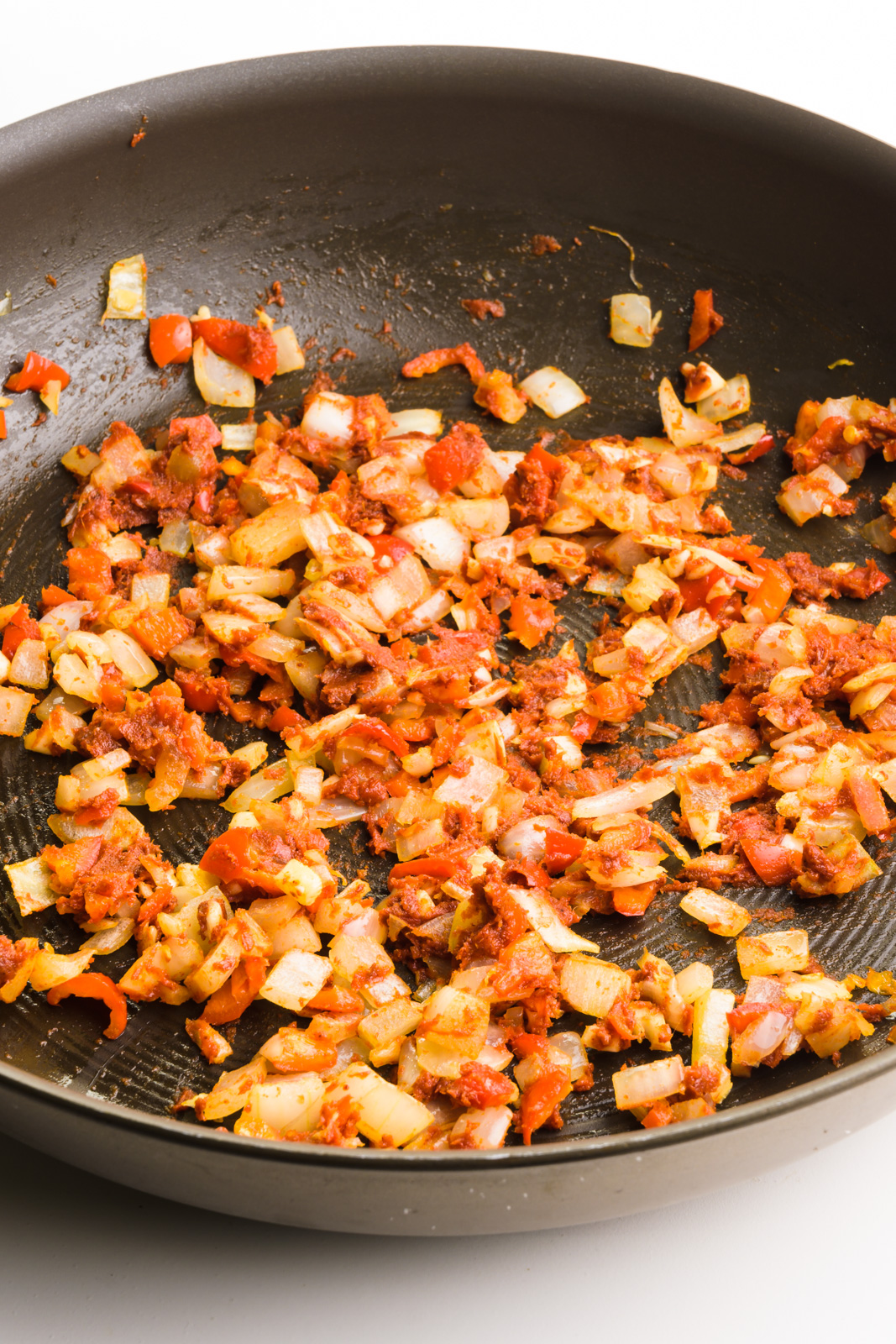 Tomato paste has been added to a vegetable mixture in a skillet.