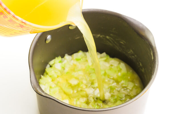 Vegetable broth is being poured into a skillet with cooked onions and celery in the bottom.