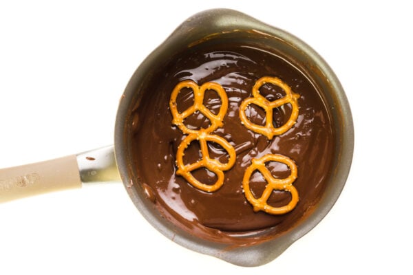 Looking down on a saucepan with melted chocolate. There are 4 pretzels on top of the melted chocolate.
