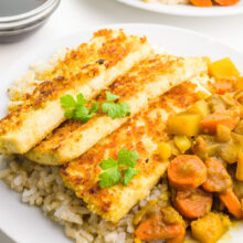 A plate has rice, fried tofu, and vegetarian katsu curry. There's a small bowl of soy sauce and another plate behind it.