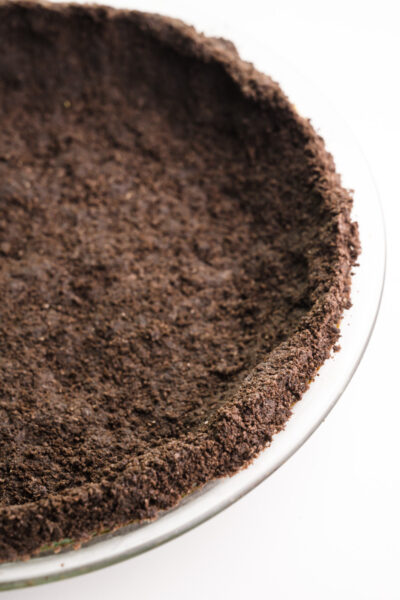 An Oreo crust has been pressed into a glass pie pan and is sitting on a white counter top.