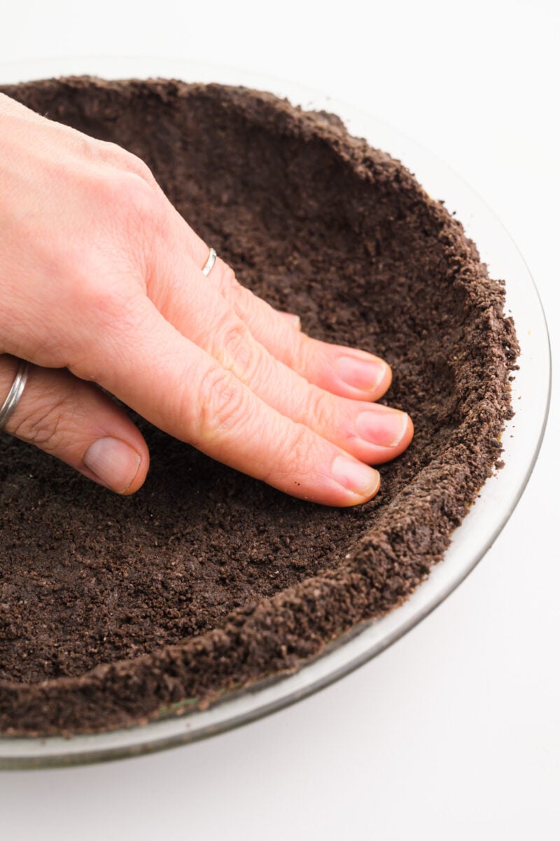 A hand presses cookie crumbs into a pie pan.