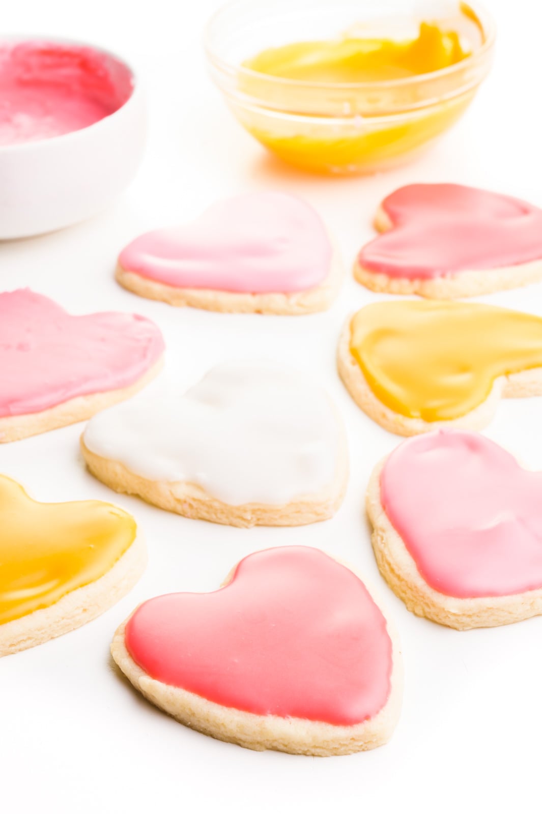 Several frosted sugar cookies have bowls of frosting behind them.
