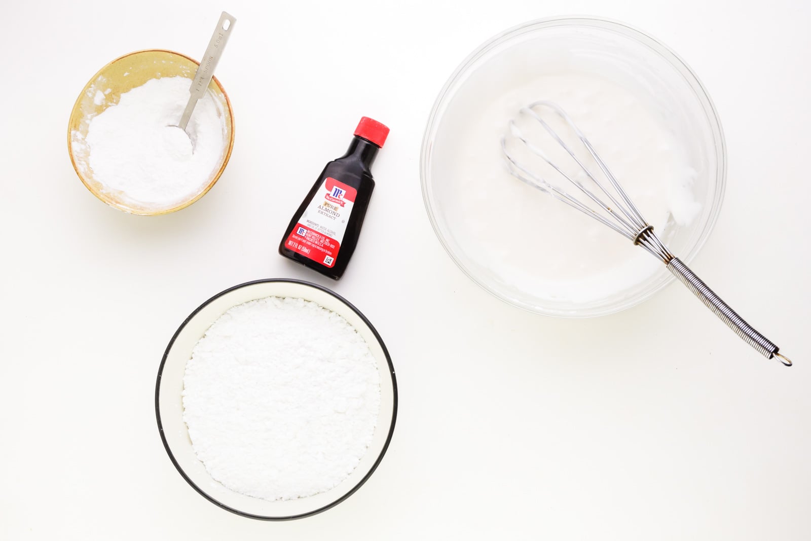 Ingredients for frosting sit on a white counter, including powdered sugar, and almond extract.