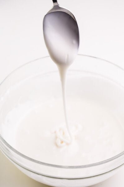 A spoon drizzles vegan royal frosting over a bowl full of more icing.