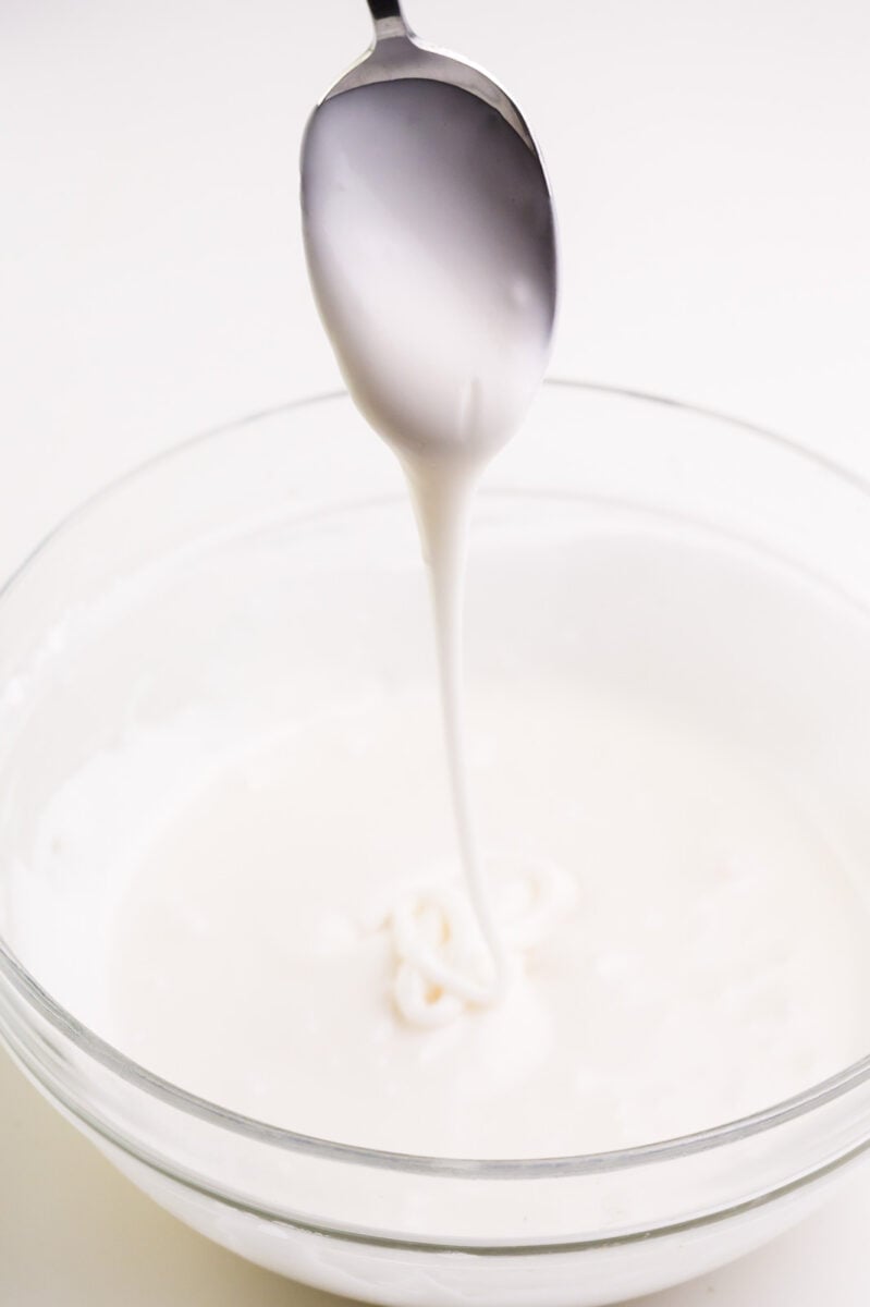 A spoon drizzles vegan royal frosting over a bowl full of more icing.