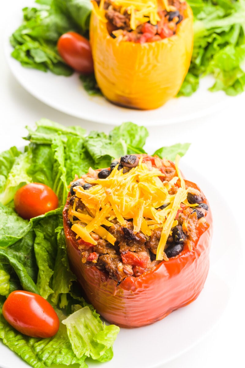 Vegan stuffed bell peppers sit on plates with salads.
