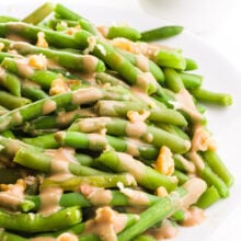 Balsamic green beans have chopped walnuts and glaze over the top. There's a bowl with walnuts in the background.