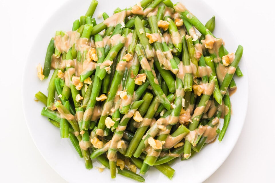 Looking down on balsamic green beans with balsamic drizzle and chopped walnuts on top.