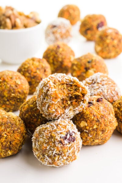 A group of carrot cake energy bites sits around a bowl of walnuts. One of the treats has a bite taken out of it.