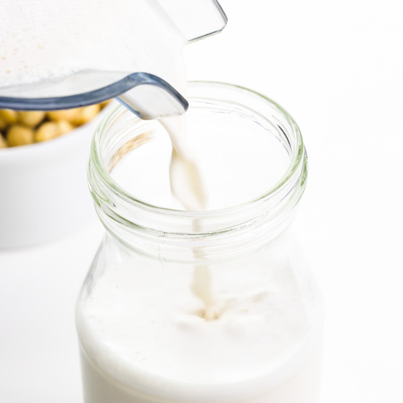 Cashew milk is being poured into a glass jar. There's a bowl of cashews behind it.
