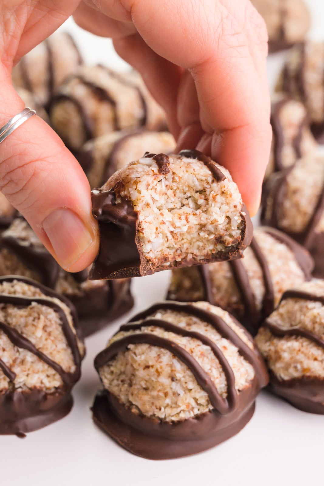 A hand holds a coconut cookie, suspended over the rest of the cookies.