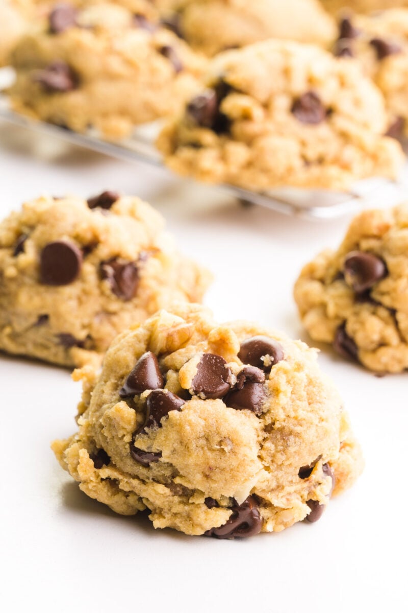 Several banana cookies are on a white counter. There are more cookies in the background on a wire rack.