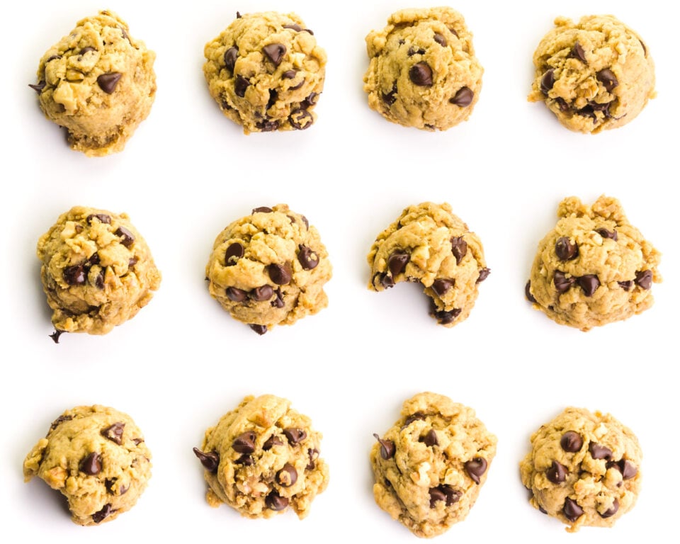 Looking down on a white try filled with chunky monkey cookies. One in the middle has a bite taken out.