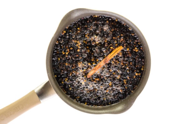 Ingredients are cooking in a saucepan with dried elderberries and a cinnamon stick.