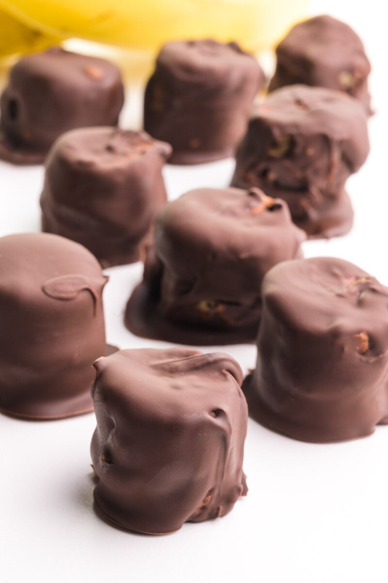 Chocolate banana bites are on a white counter. There are bananas in the background.