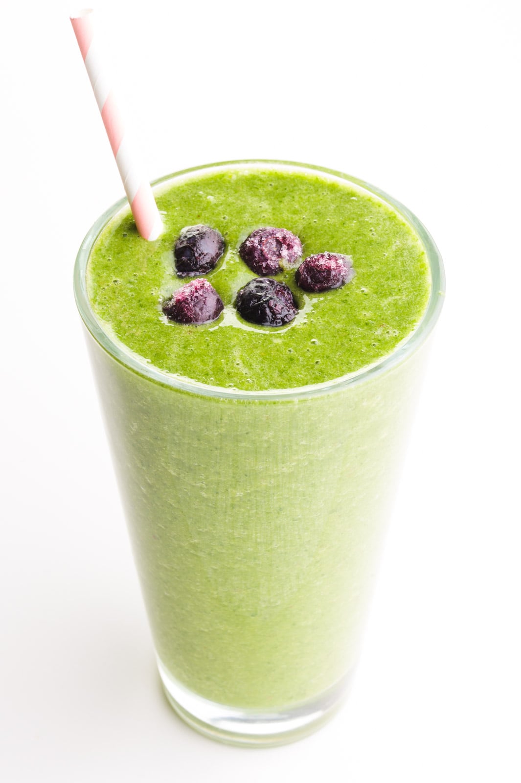 A green smoothie has blueberries on top and a pink straw on the side.