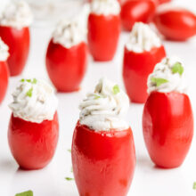 Stuffed cherry tomatoes are on a white serving tray with bits of fresh parsley around it.