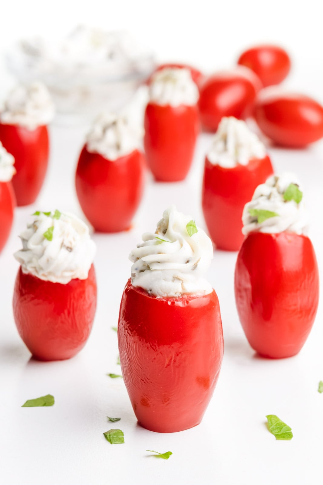 Stuffed cherry tomatoes are on a white serving tray with bits of fresh parsley around it.