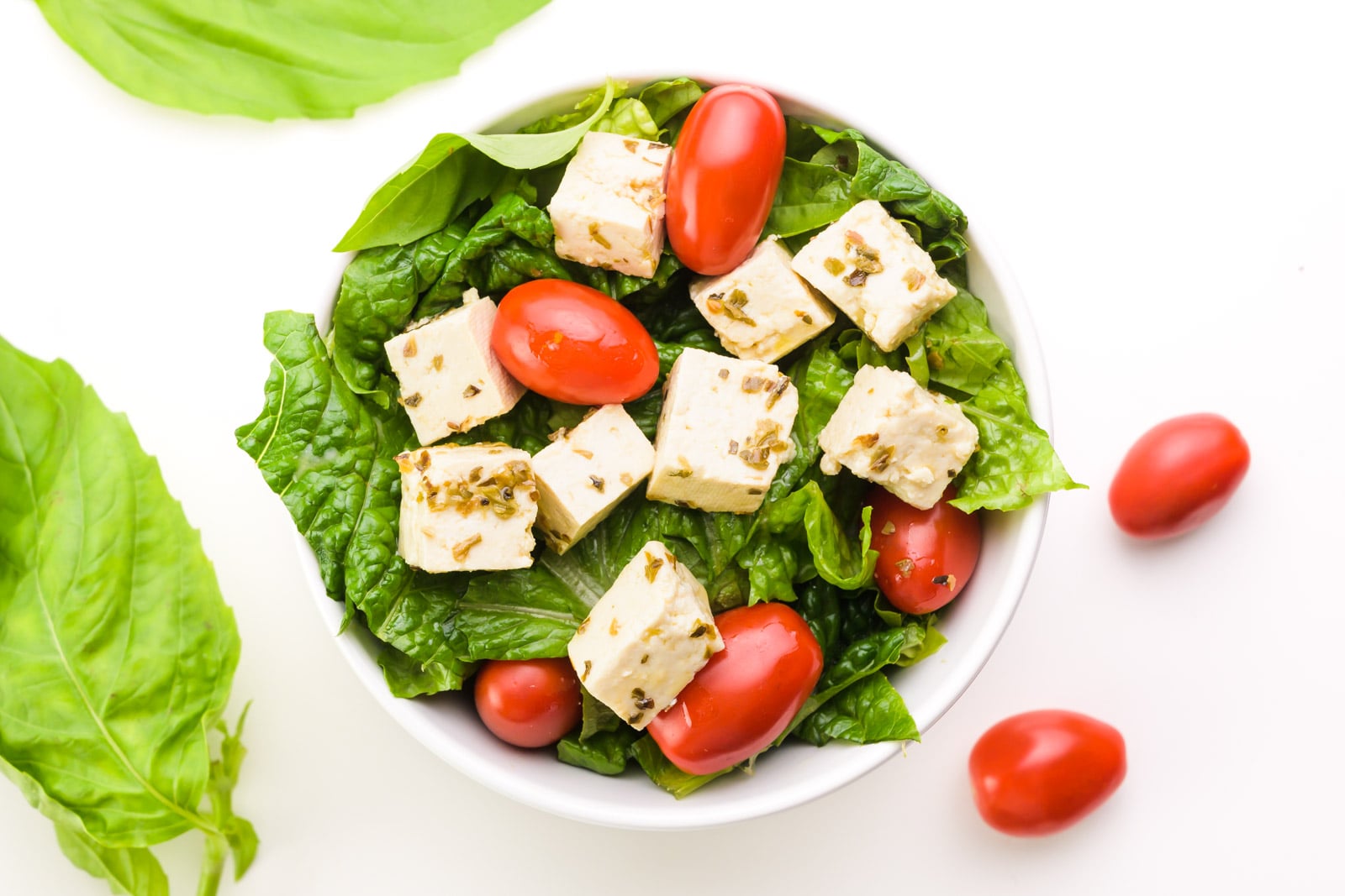A bowl holds lettuce, cherry tomatoes, and cubes of tofu feta.