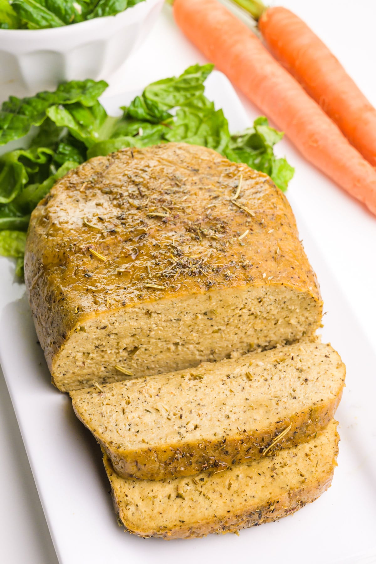 Looking down on a vegetarian turkey loaf with greens and carrots behind it.