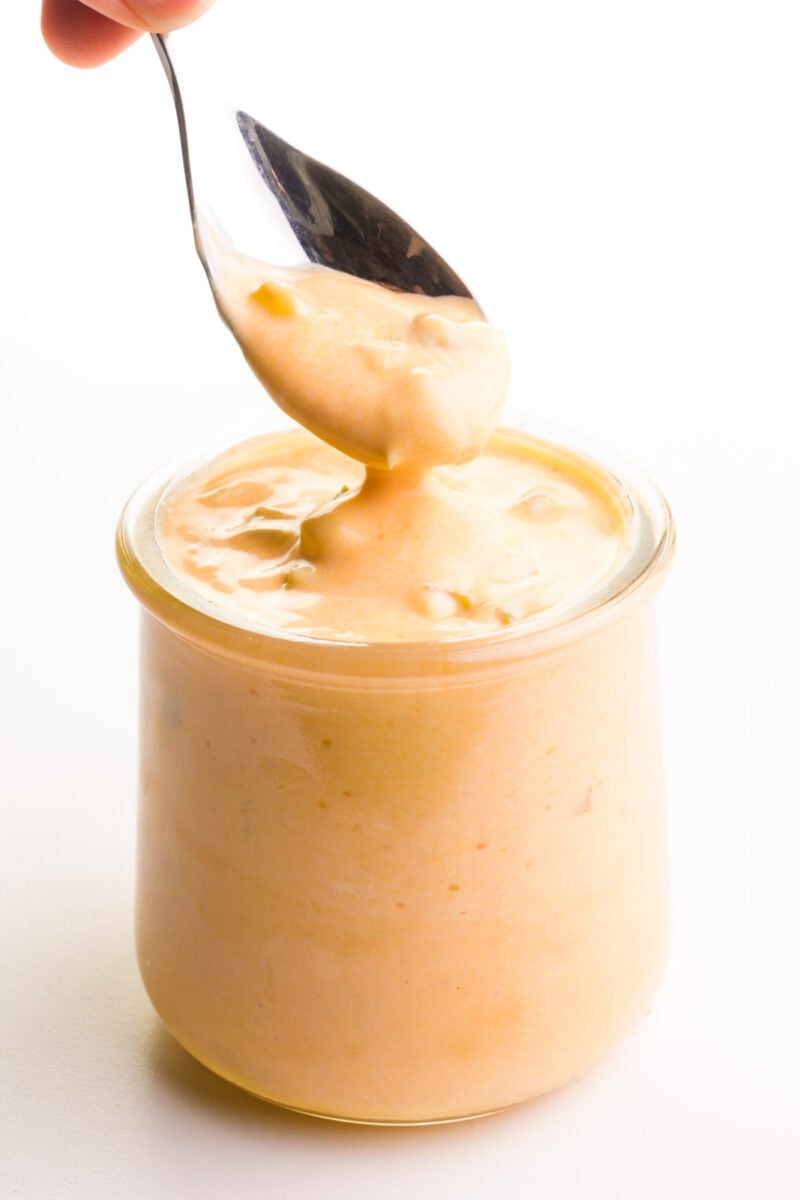 A hand holds a spoonful of vegan Big Mac sauce over a jar with the sauce.