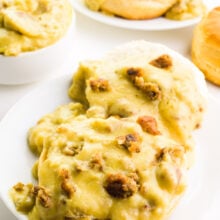 A plates holds vegan biscuits and gravy. There's a bowl with more gravy behind it along with biscuits and another plate of the dish.