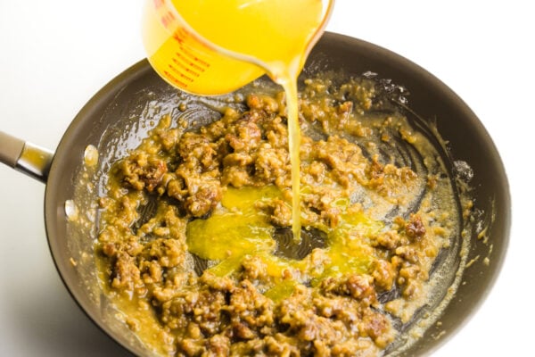 Broth is being poured into a skillet with a roux to create gravy.