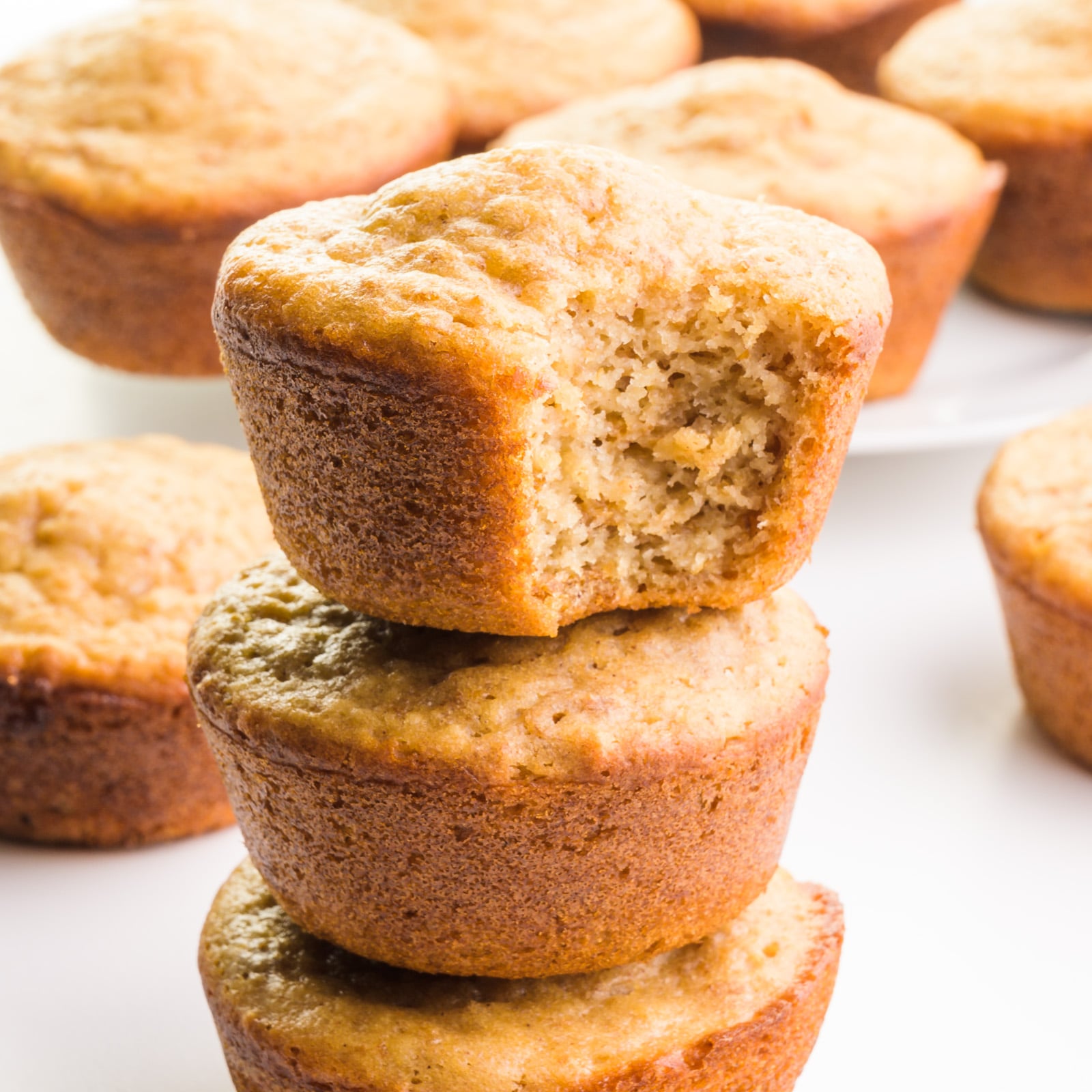 A stack of muffins shows the top one with a bite taken out. There are more muffins in the background.