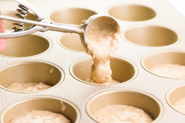 A cookie scooper is distributing batter into a muffin tin.