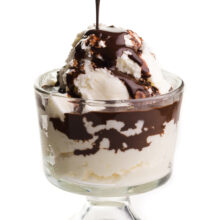 a spoon of chocolate sauce drizzling over vanilla ice cream in a dessert bowl