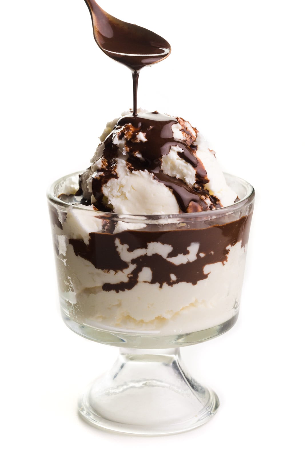 a spoon of chocolate sauce drizzling over vanilla ice cream in a dessert bowl