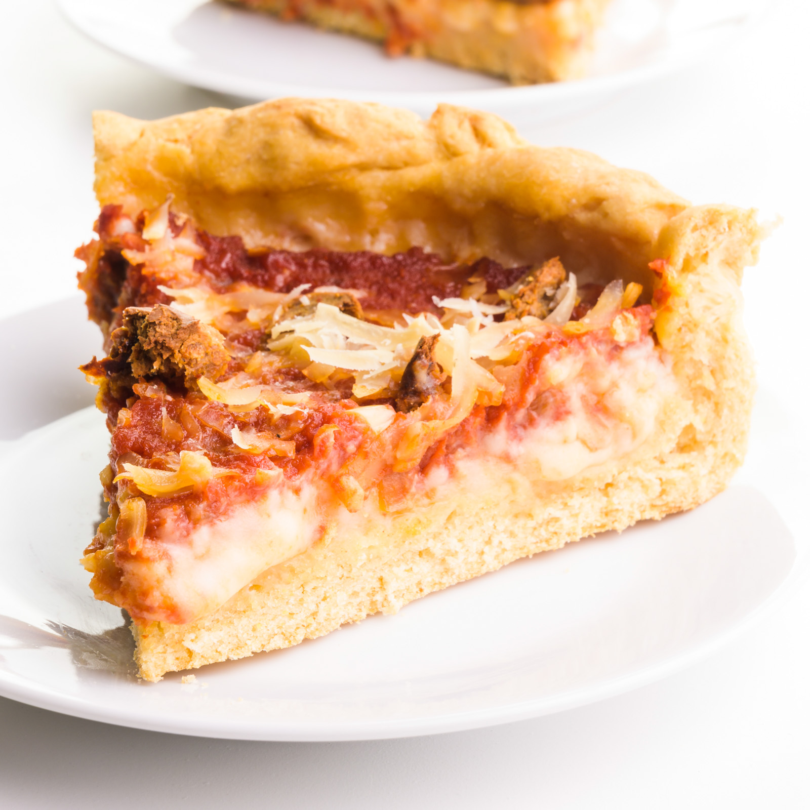 A slice of deep dis pizza sits on a plate, showing cheese melting from the side.