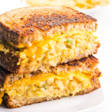 A vegan tuna melt sandwich is cut and half and the two halves are stacked, revealing melted vegan cheese and chickpea tuna salad.