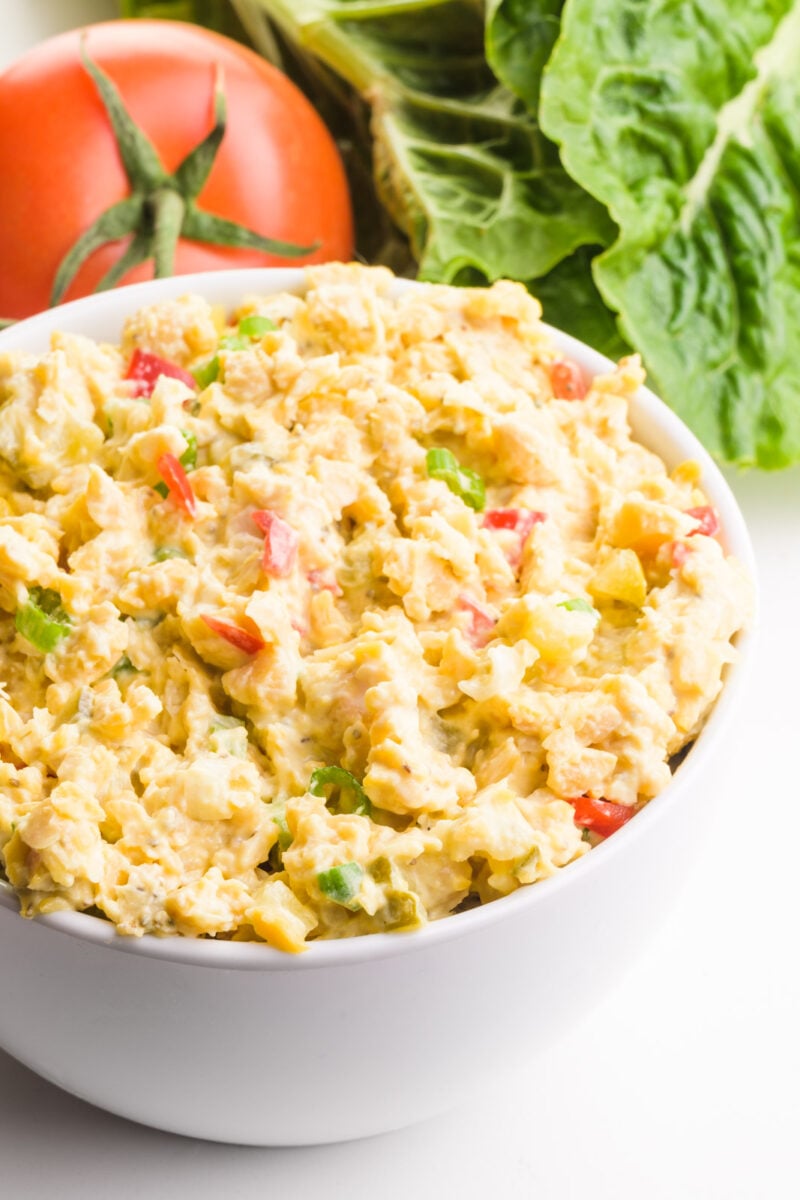 A bowl of vegan tuna salad has leafy green lettuce and a tomato in the background.