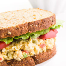 A vegan tuna salad sandwich has lettuce and sliced tomatoes on it. There's a bowl of potato chips in the background.