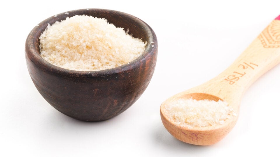 A wooden bowl an da wooden measuring spoon are full of agar agar flakes.