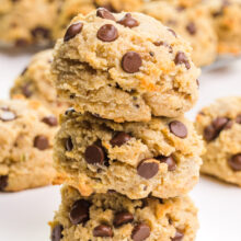 A stack of three almond flour cookies showcase lots of chocolate chips. there are more cookies in the background.